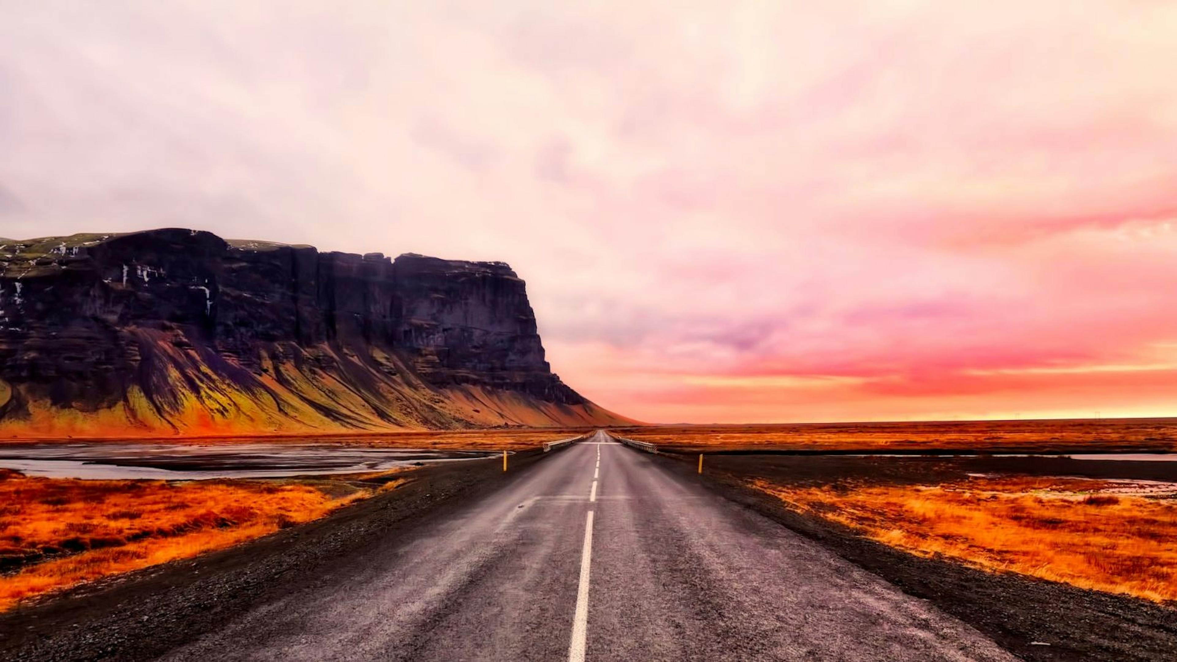 A highway in Iceland during a pink sunset with mountains in the background.