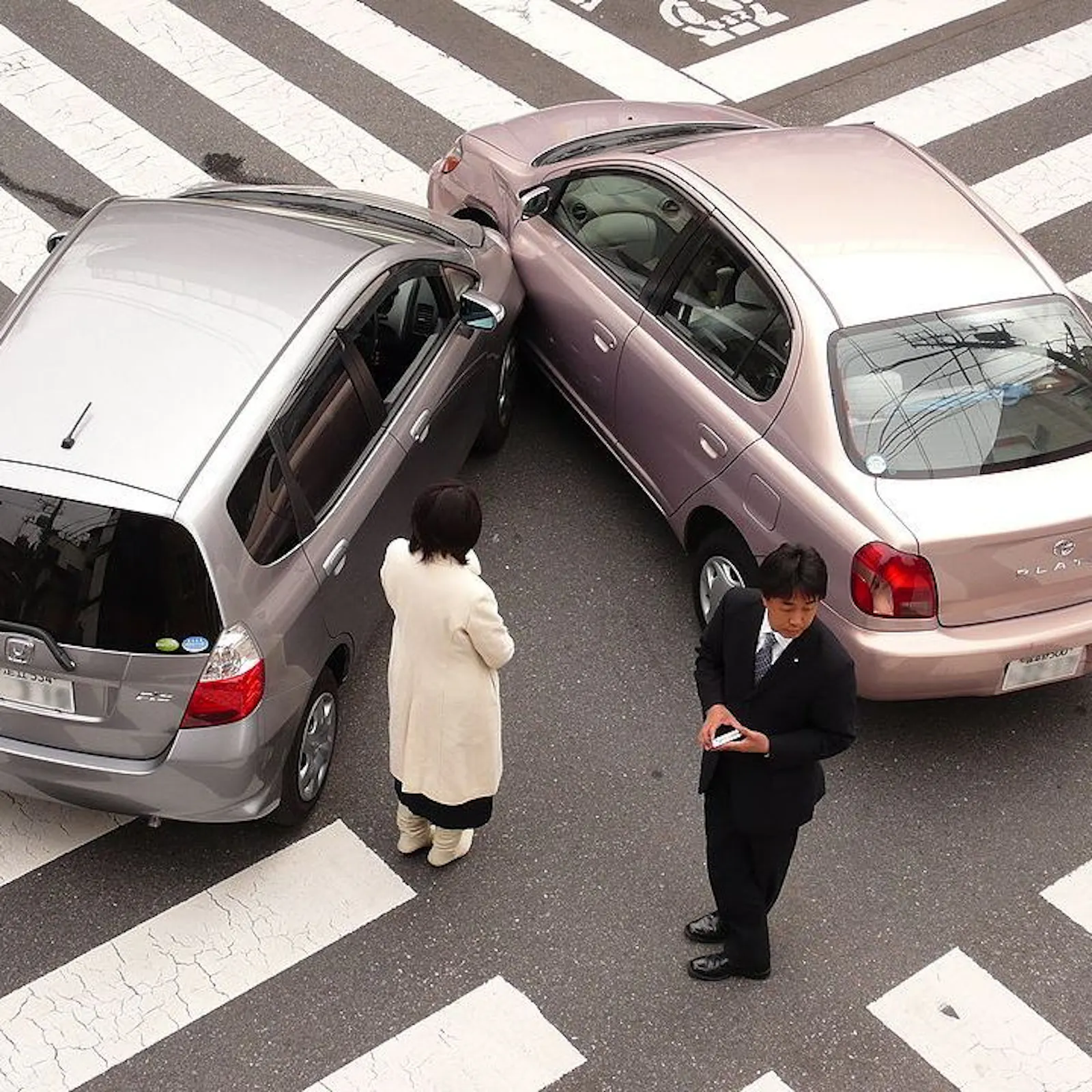 2 cars that have collided and their drivers stood on the road