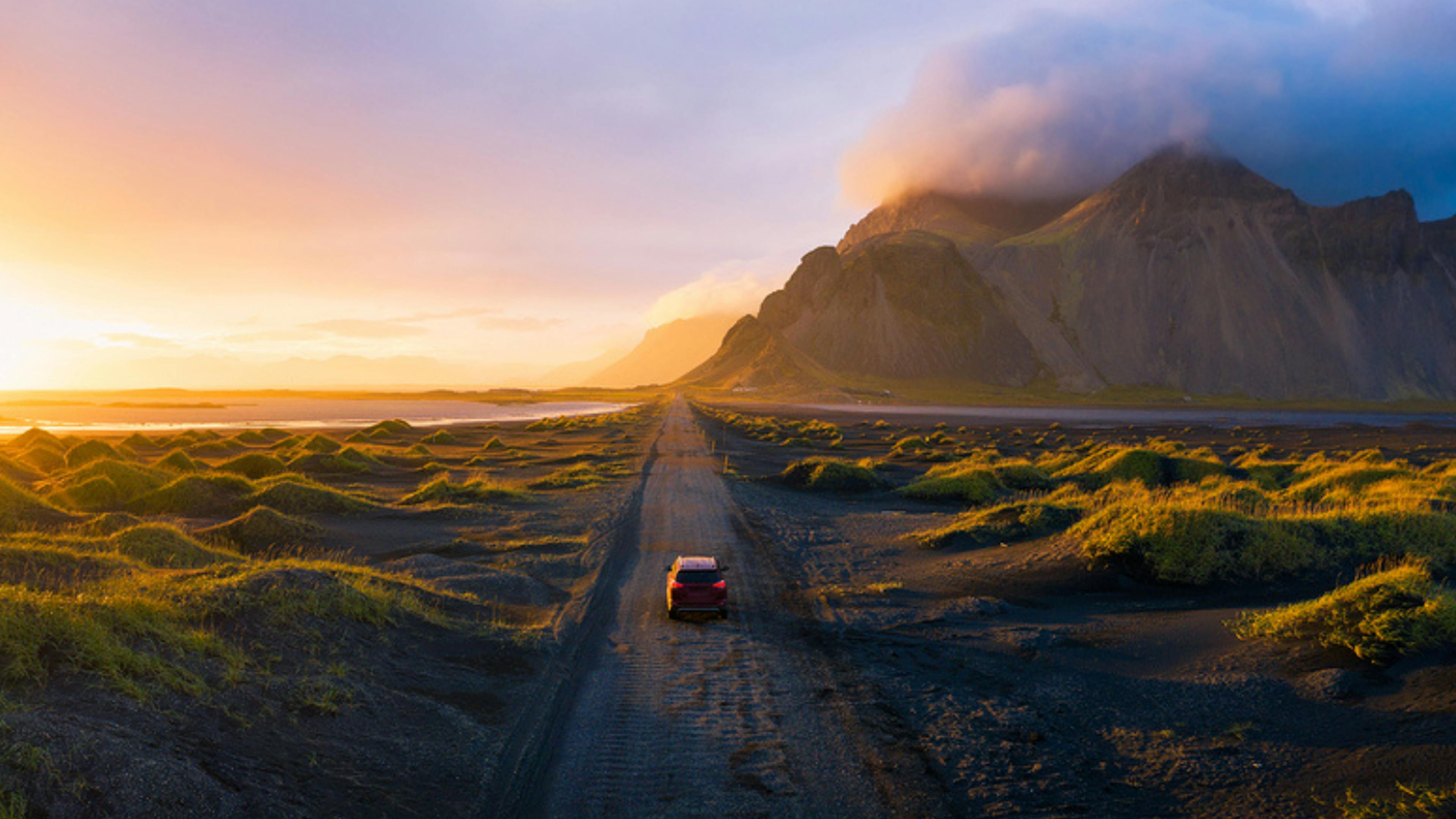 Car driving on a gravel road towards Vestrahorn Mountain in Iceland at sunset