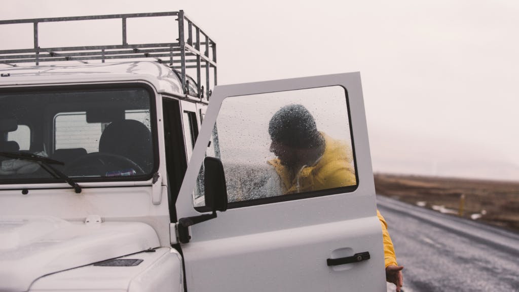 Man road-tripping through Iceland leaning into a car in the rain.