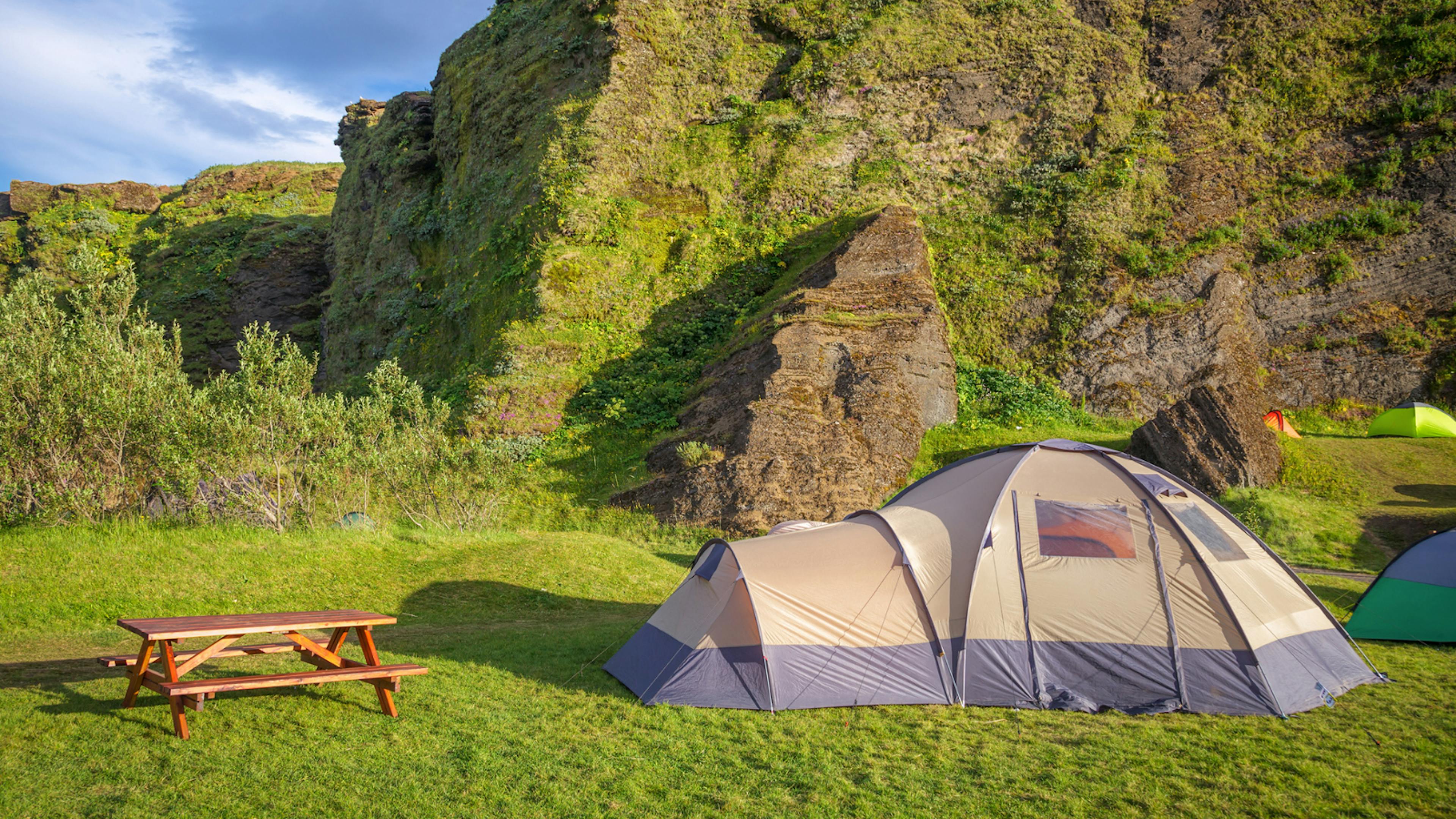 Large dome tent pitched next to a wooden picnic bench in green Icelandic scenery.