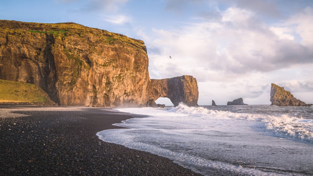 Dyrhólaey beach in Iceland with black sand and rock formations.
