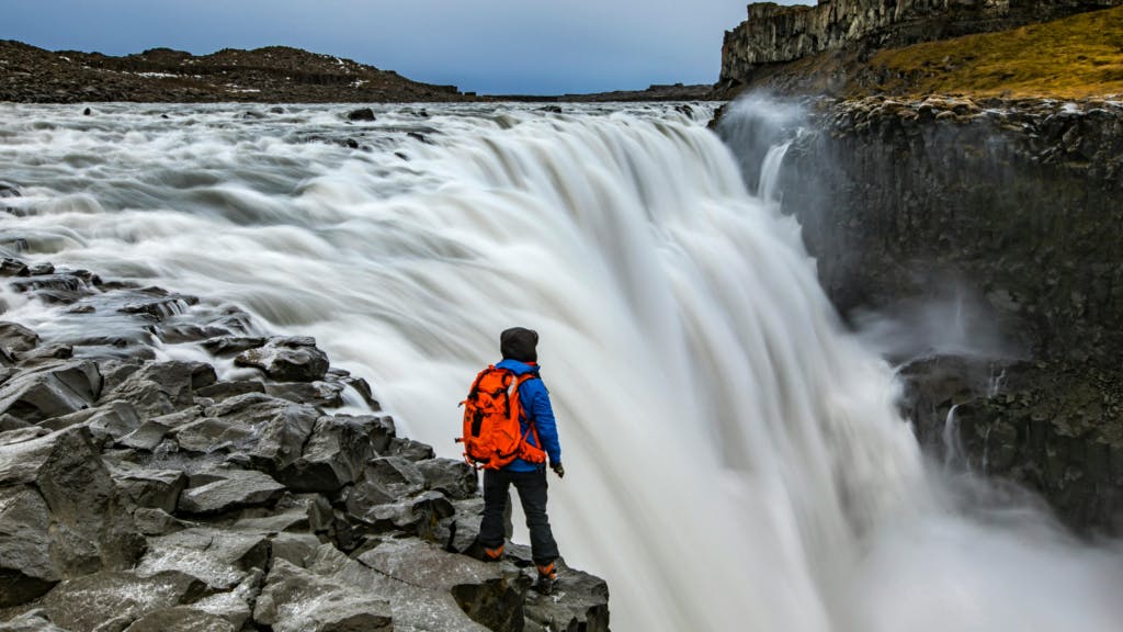 Person standing along the rocks at Dettifoss waterfall.