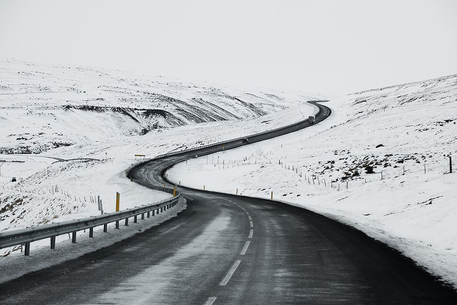 An S-shaped asphalt road in Iceland in the winter with sidewalks full of snow