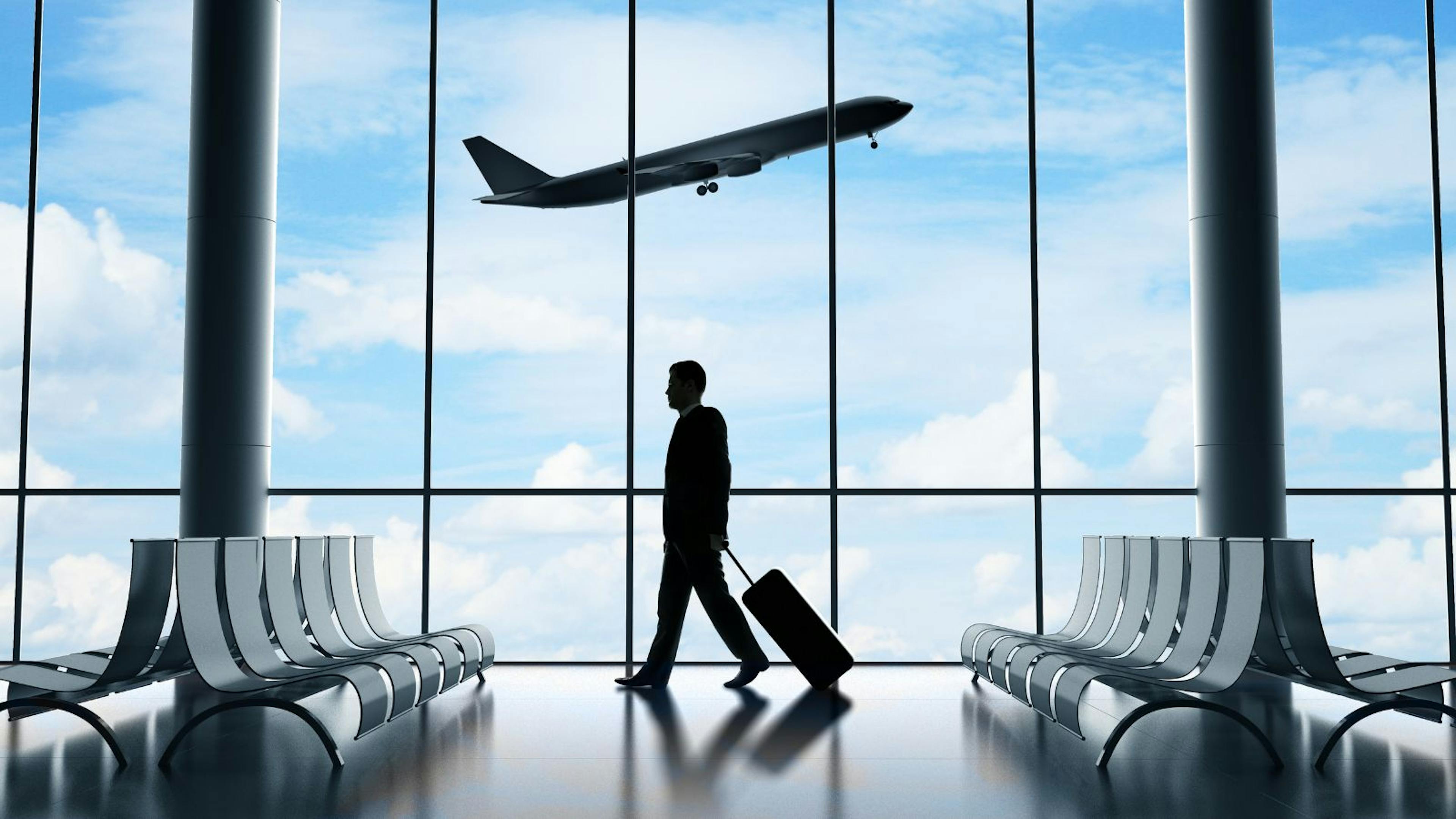 A traveler in an airport with an airplane taking off in the background