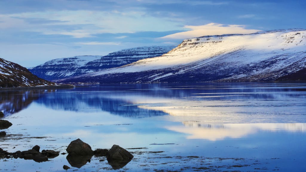Snowy mountains reflecting in the fjords of the Westfjords in Iceland.