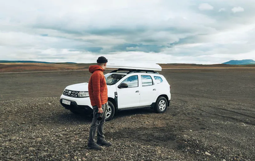 Man holding a camera stood in front of a white Dacia gravel in Iceland