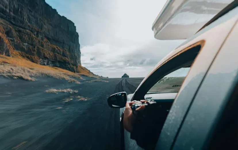 Passenger holding a camera out the window of a driving car on a mountain road in Iceland
