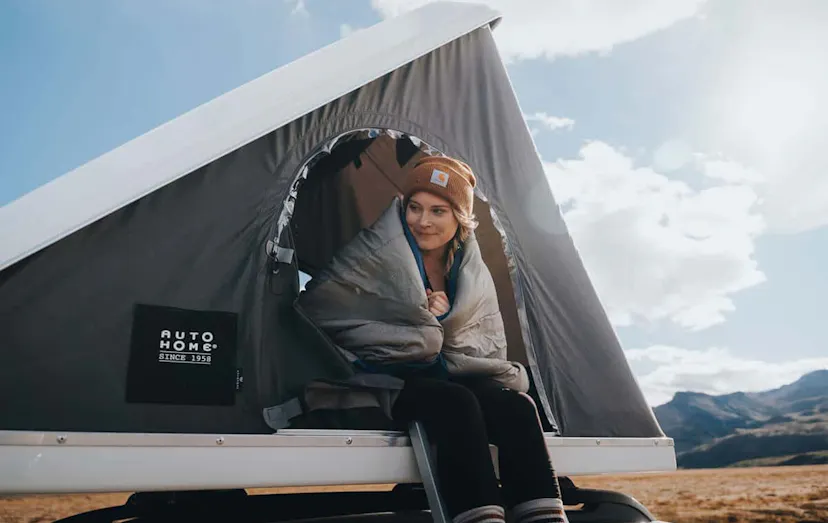 Lady wrapped in a sleeping bag, sitting in a pop up tent on top of a car in Iceland