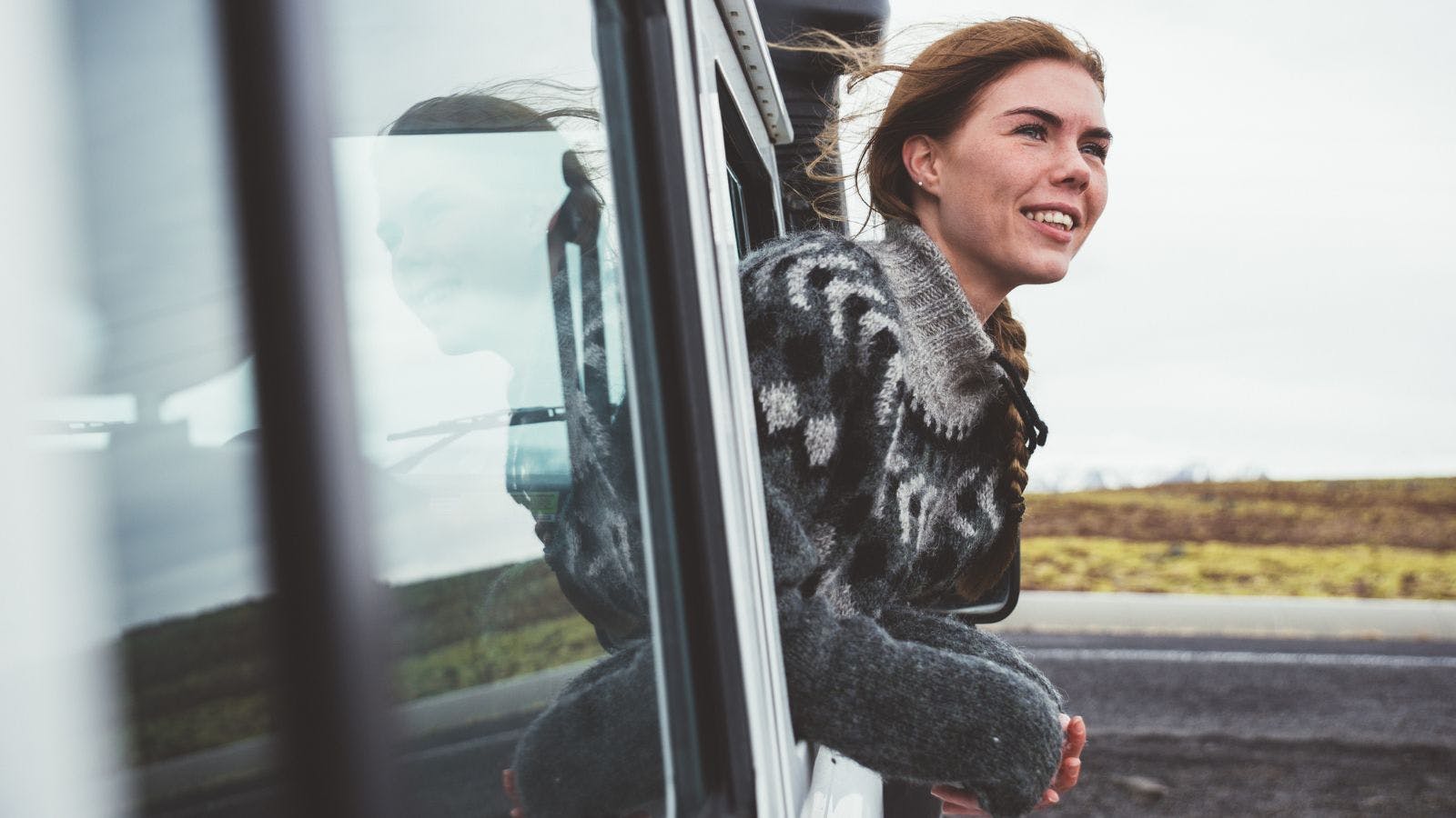 Woman in an Icelandic jumper leaning out of the car window on the side of the road.