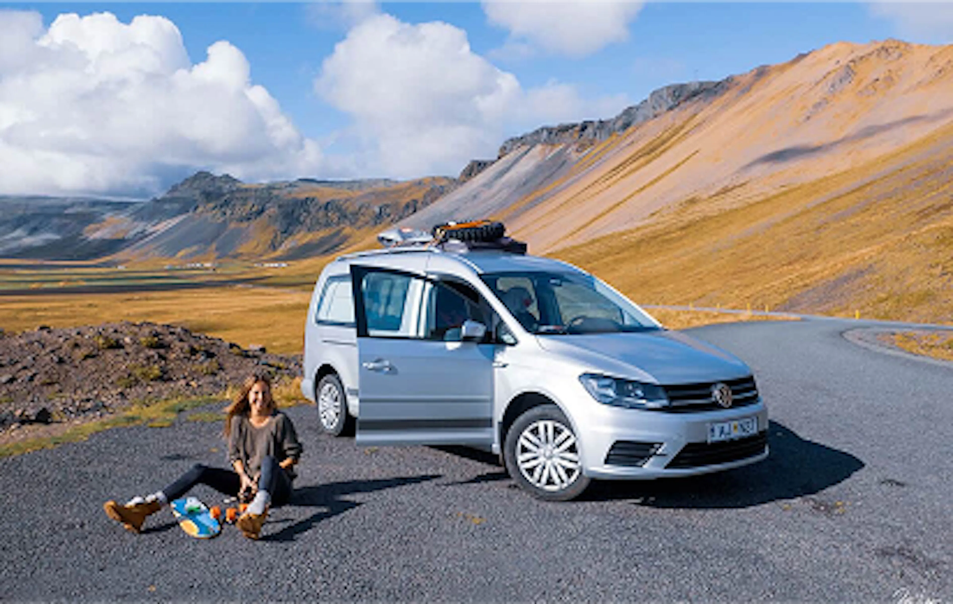 A lady sitting on a gravel road next to a VW camper in Iceland