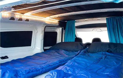 2 blue sleeping bags set up inside the back of a camper