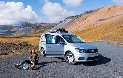 A lady sitting on a gravel road next to a VW camper in Iceland