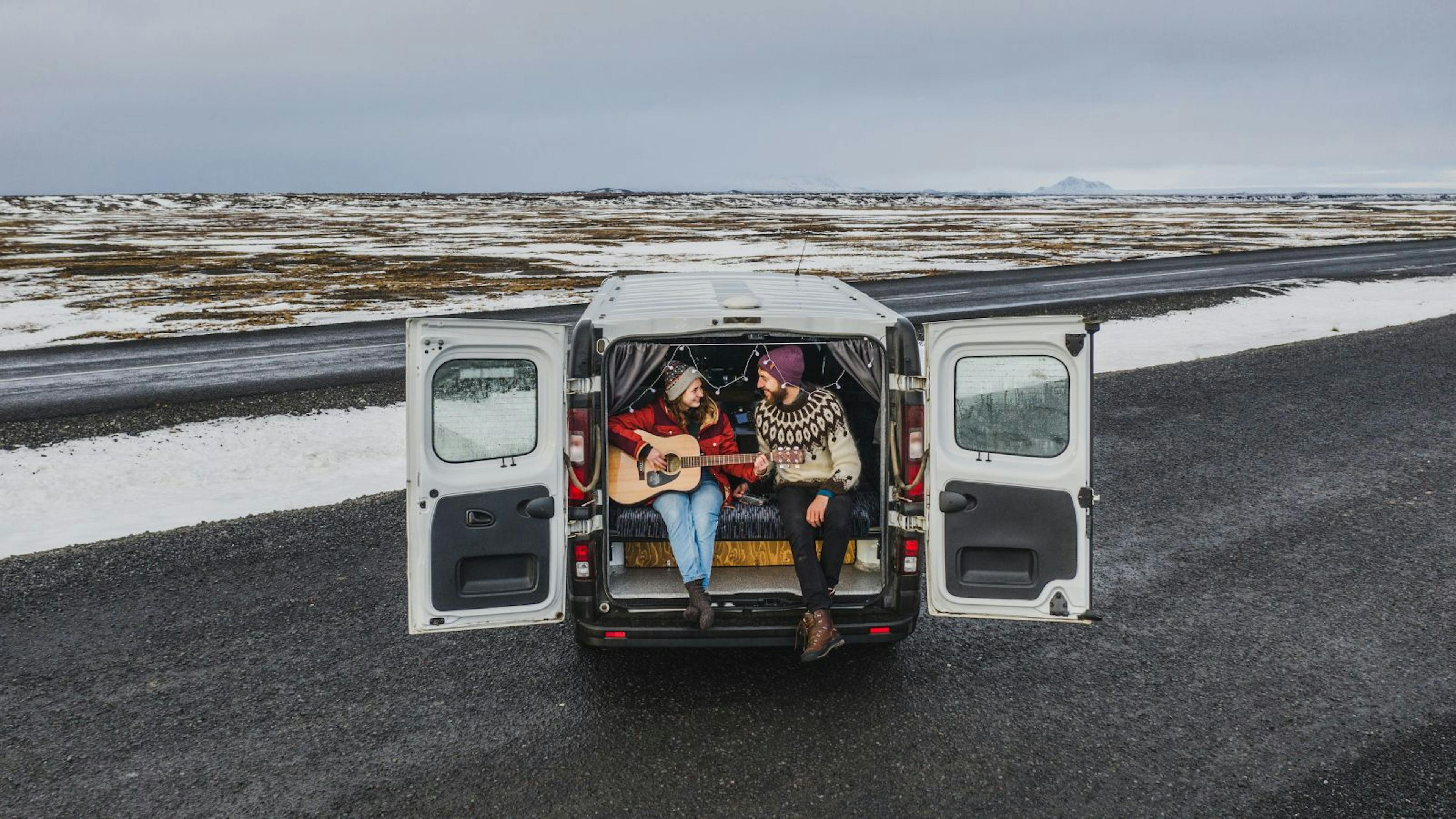 Couple in the back of a motorhome playing guitar on a road in Iceland.
