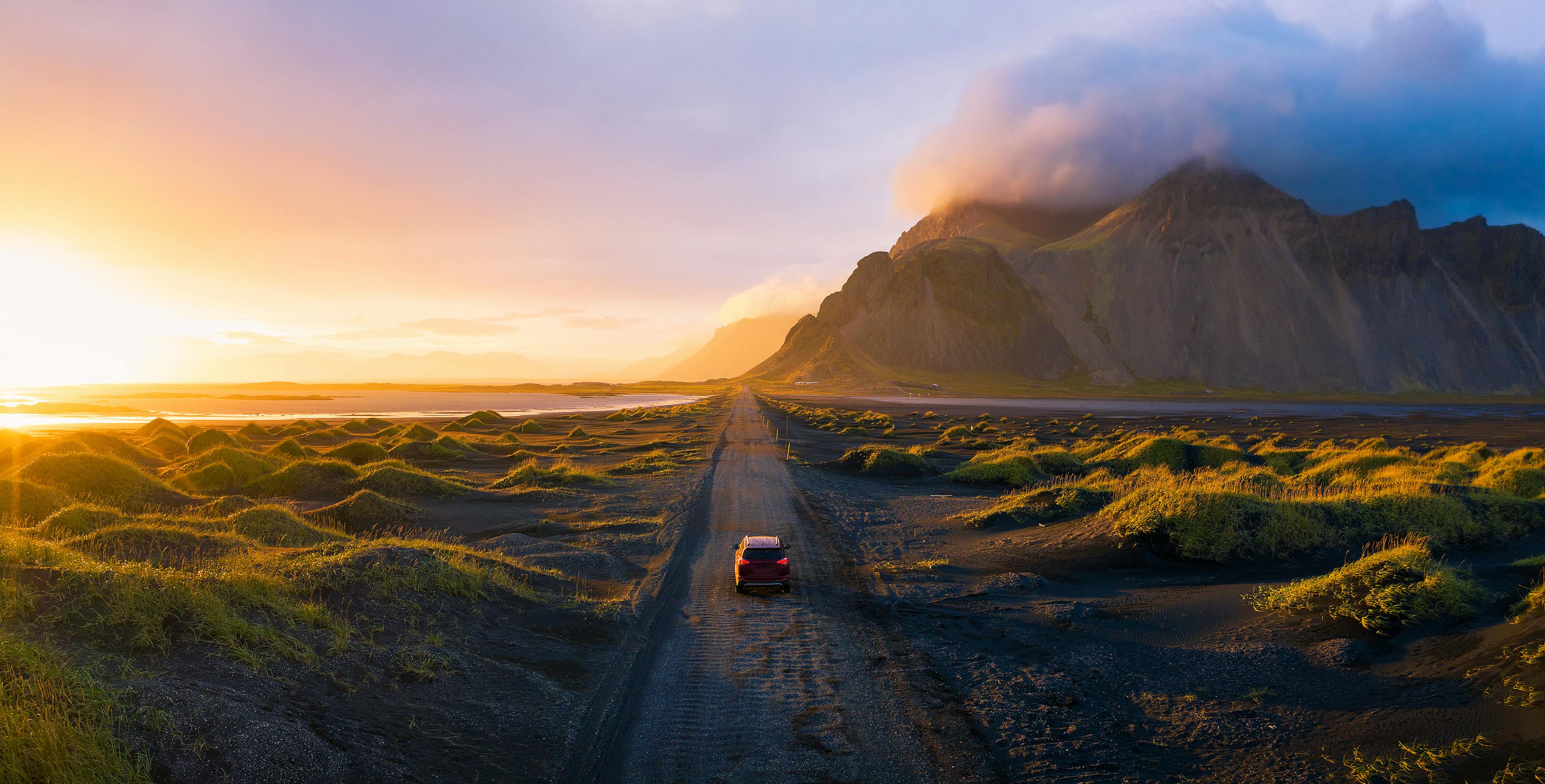 Car driving on the gravel road to Vestrahorn Mountain at sunset.