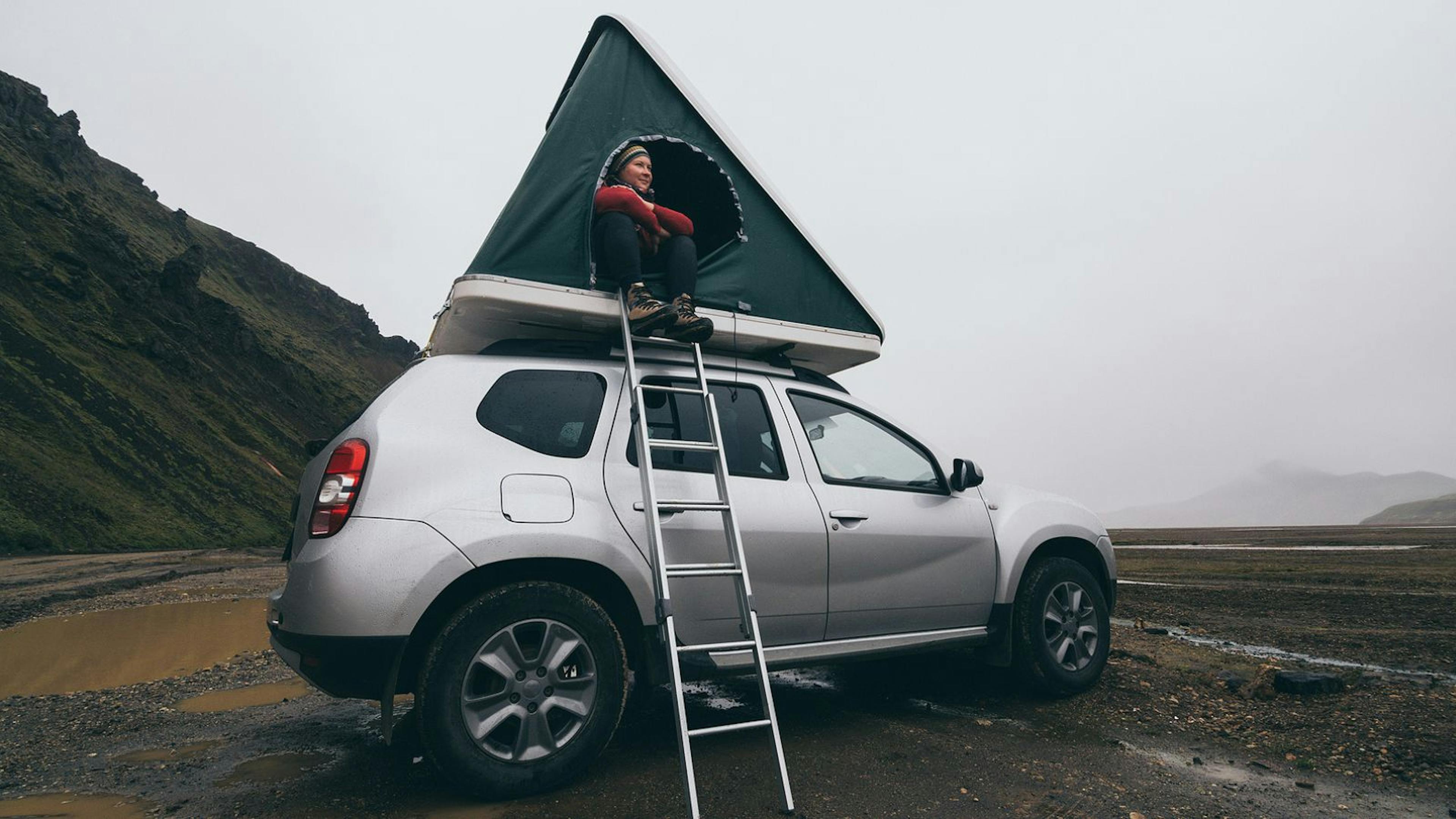 Woman sitting in the tent of a rooftop tent camper in Iceland.
