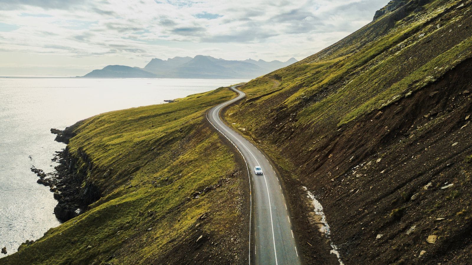 Dramatic views of a winding coastal road in Iceland with a single car on it.