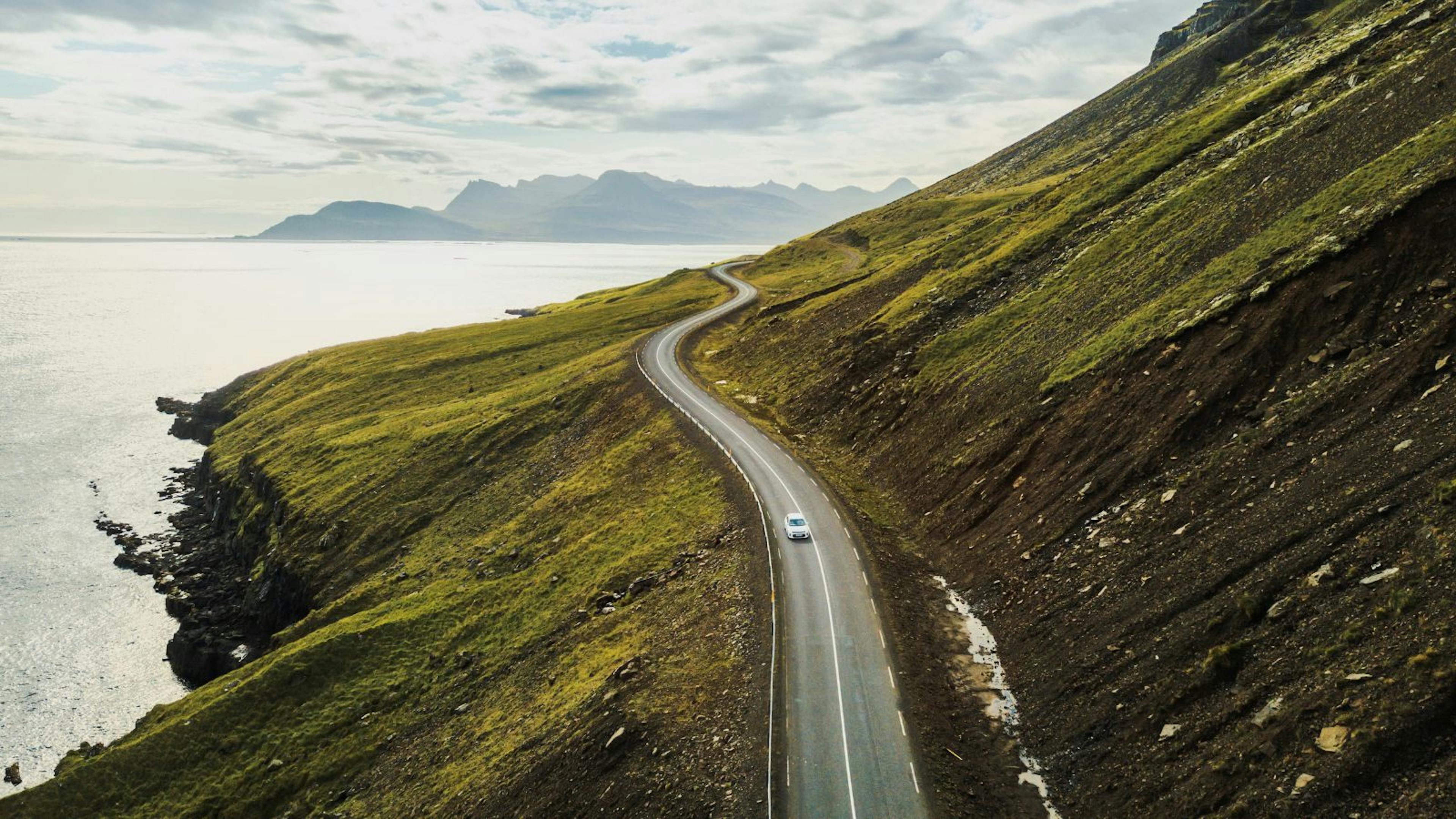 Dramatic views of a winding coastal road in Iceland with a single car on it.
