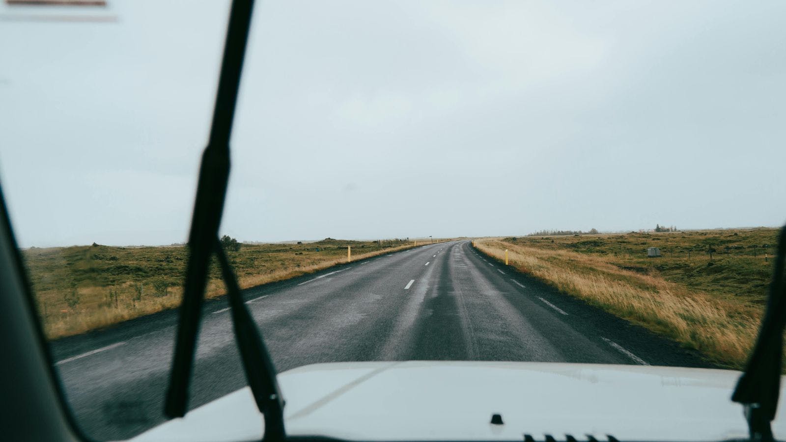 Looking out the windscreen of a vehicle at a road in Iceland with the windshield wipers on.