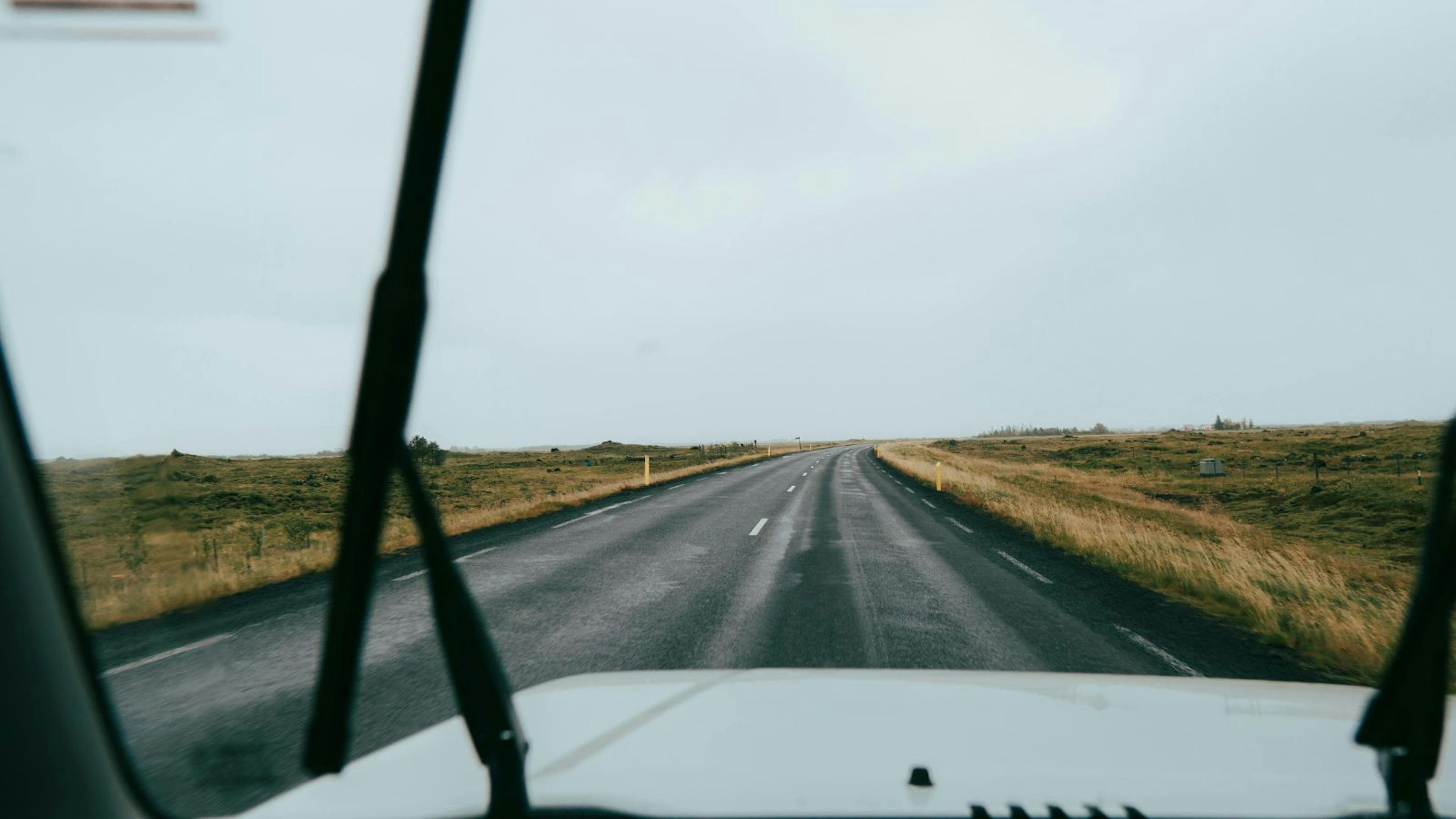Looking out the windscreen of a vehicle at a road in Iceland with the windshield wipers on.