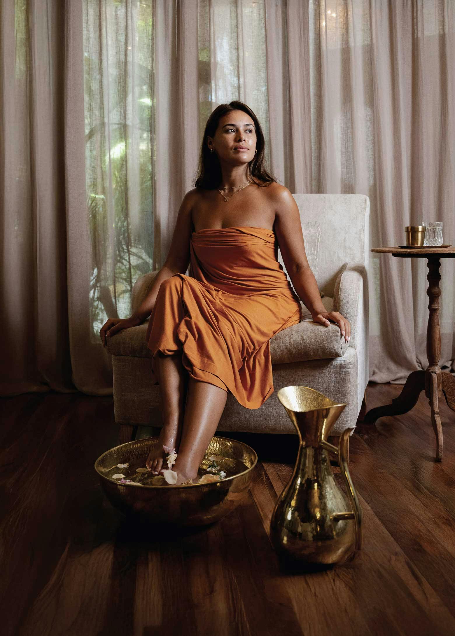 Woman in a luxurious spa room with a flower-filled foot bowl below her.