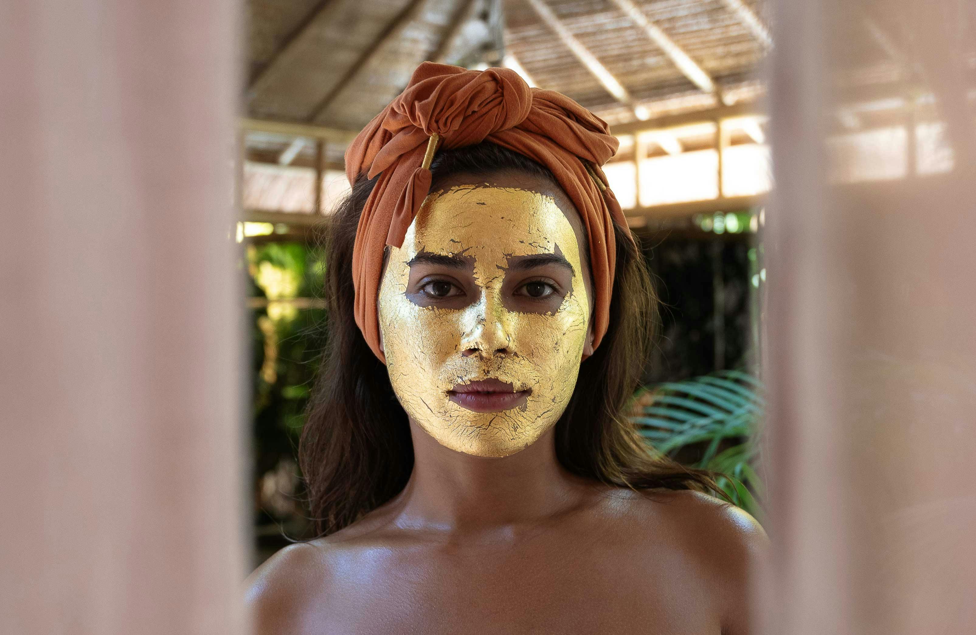 woman standing behind curtains with a 24k gold facial