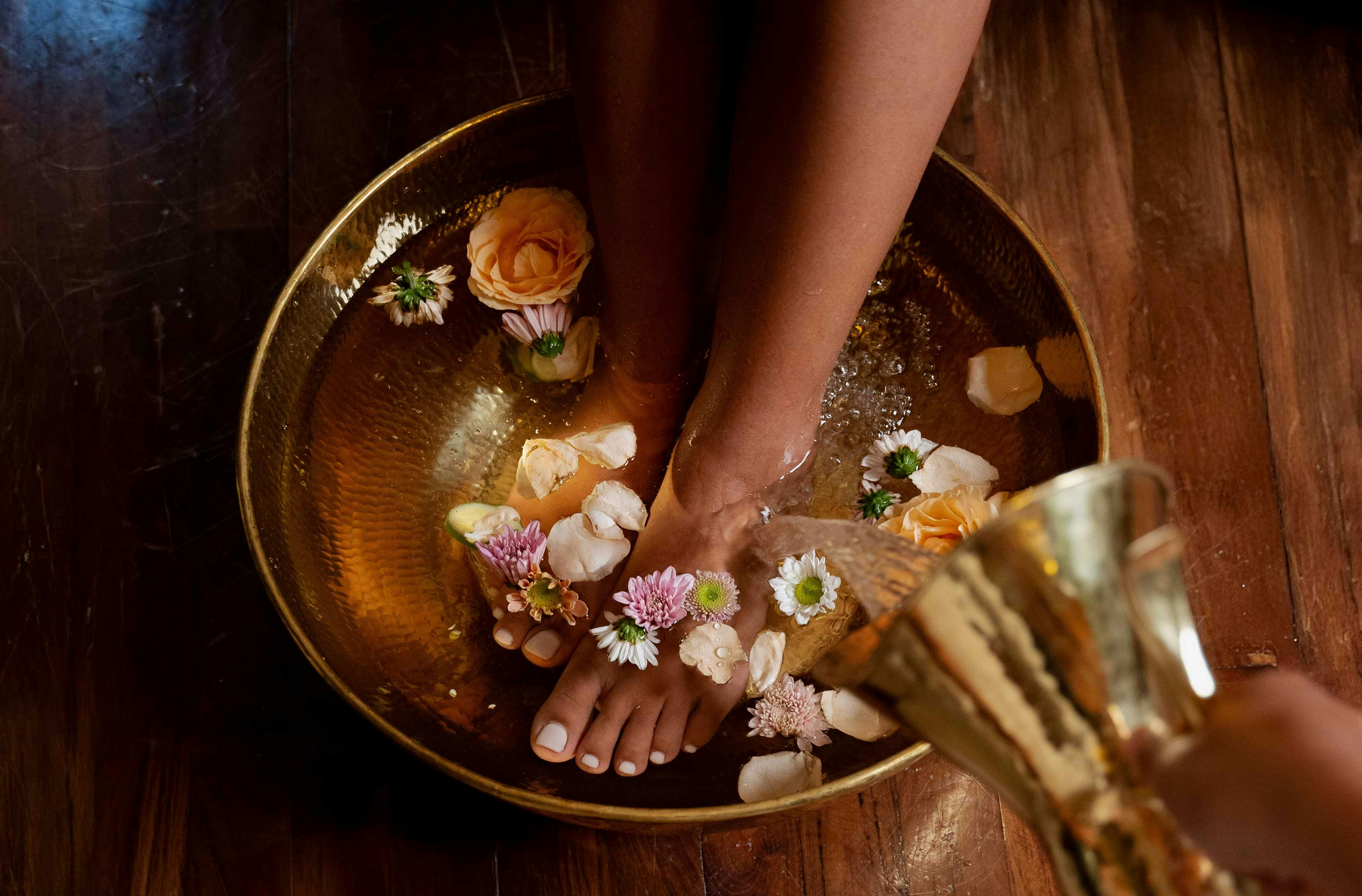 Woman's feet in a golden bowl filled with flowers.