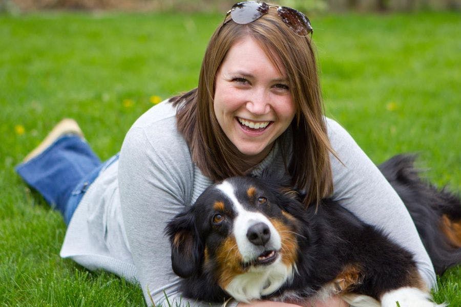 Smiling woman laying in grass hugging smiling dog