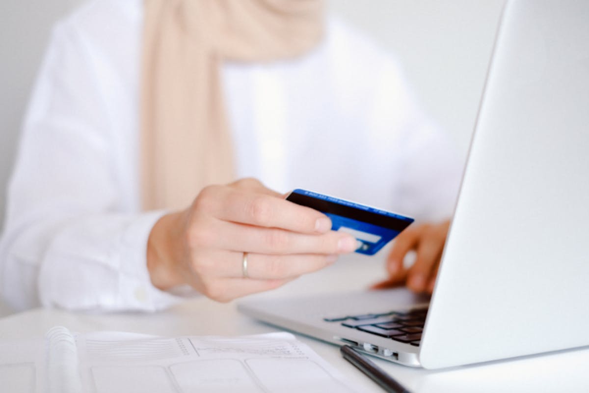 A person holding a credit card next to a computer