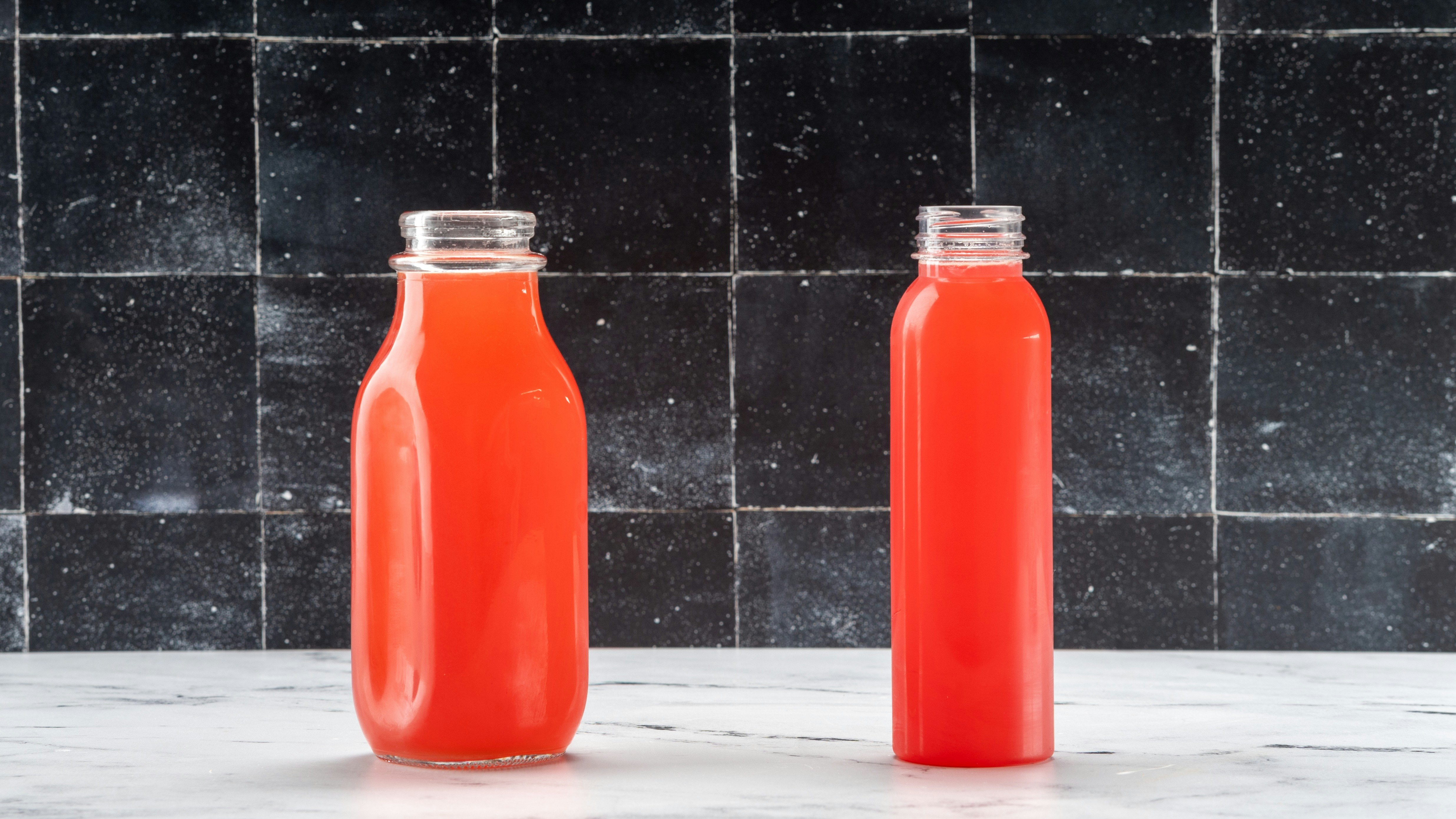 Glass juice bottle next to plastic juice bottle on dark background