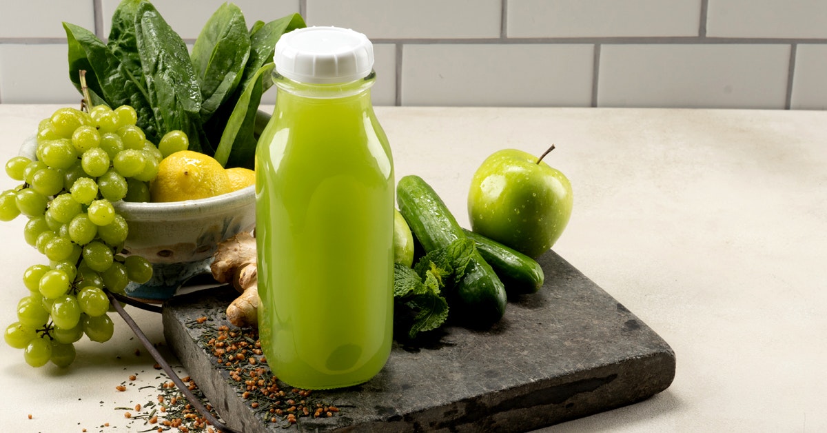 bottle of green juice with ingredients grapes, spinach, green tea, cucumber, mint, lemon and green apple on a countertop