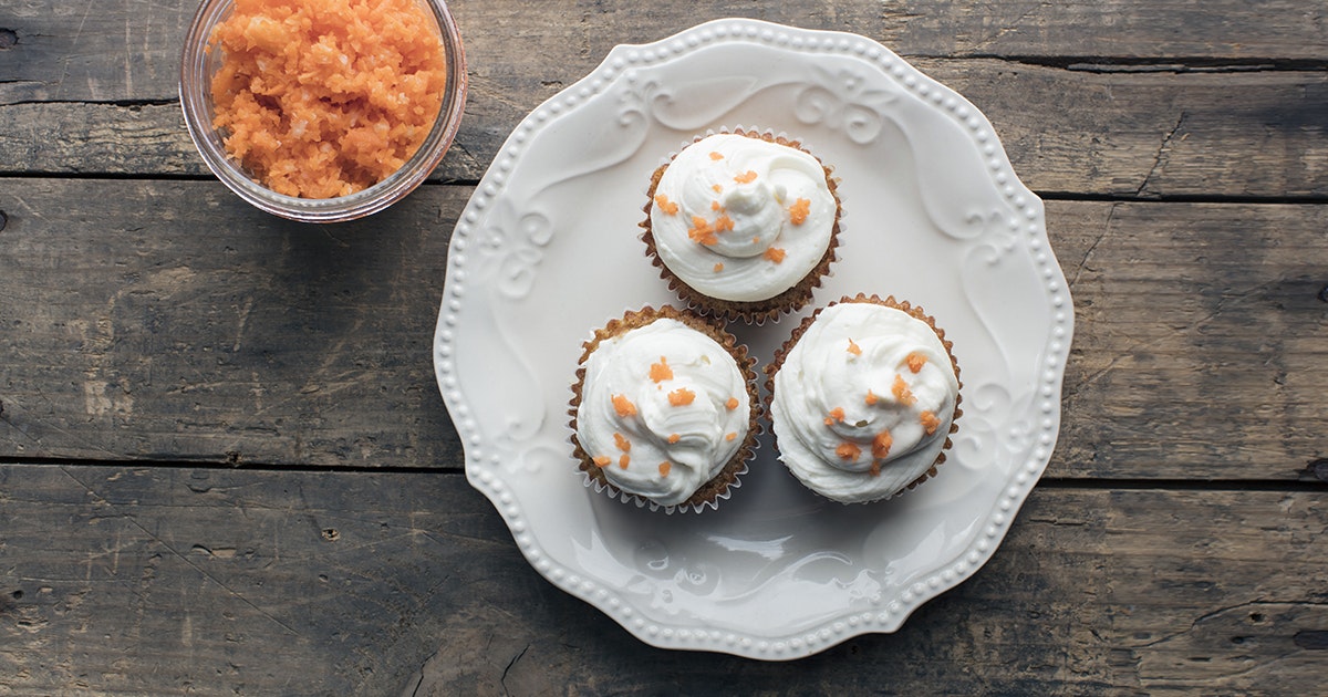 three cupcakes on a white plate next to carrot juice pulp