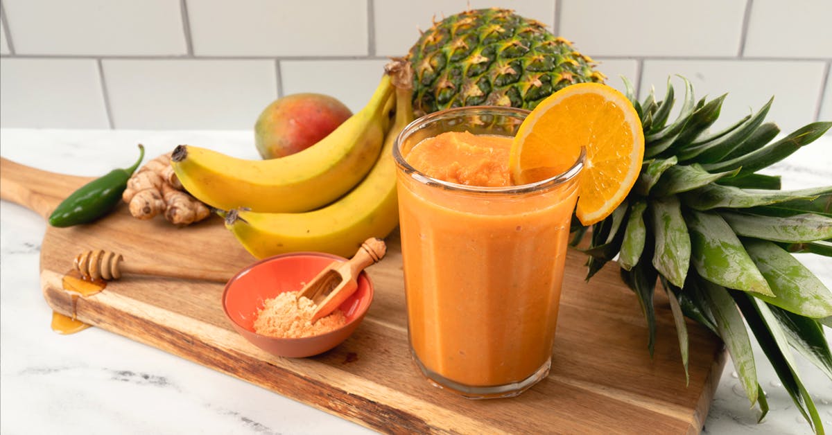 tropical maca smoothie on a wooden cutting board with pineapple, banana, ginger, maca root powder and mango