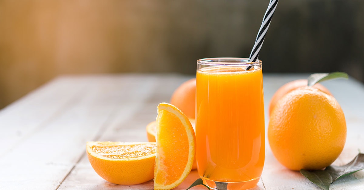 does orange juice have calcium? a glass of OJ on a table with a straw next to sliced and whole oranges