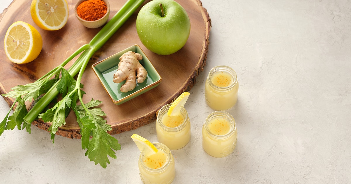 four juice shots with ingredients on a wood cutting board