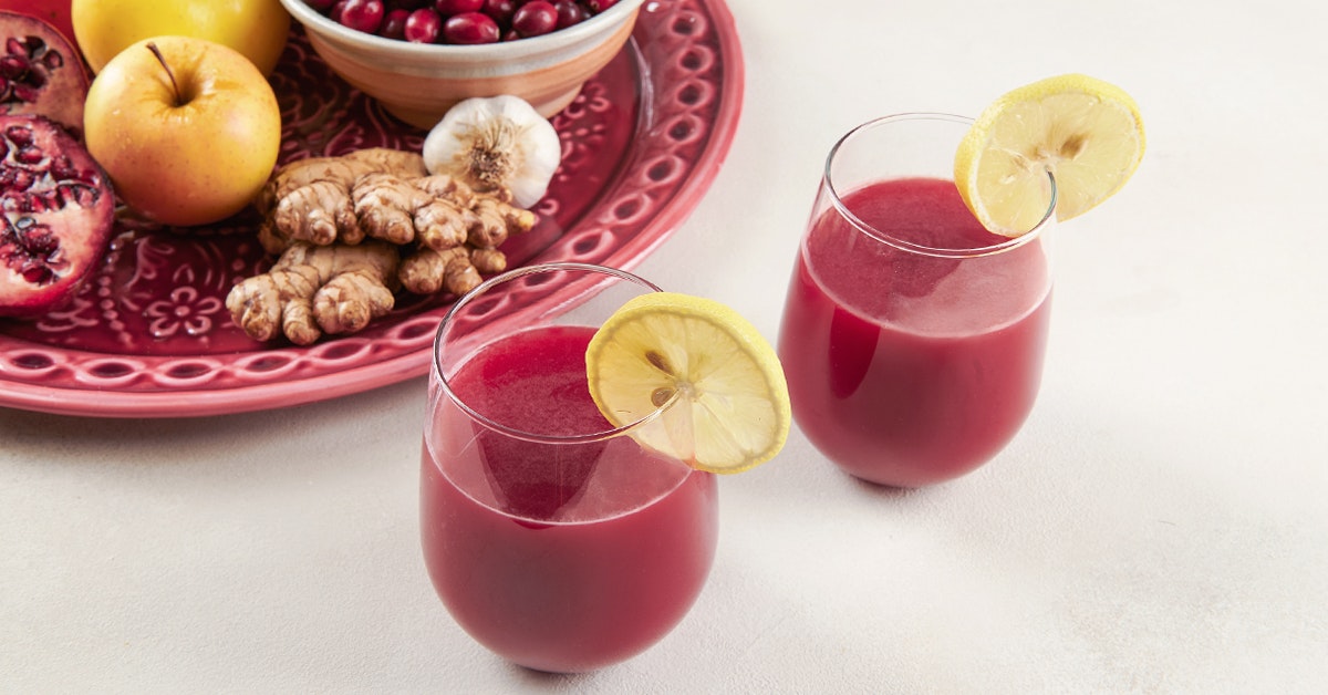 two glasses of pomegranate and cranberry juice with a lemon slice on a white surface