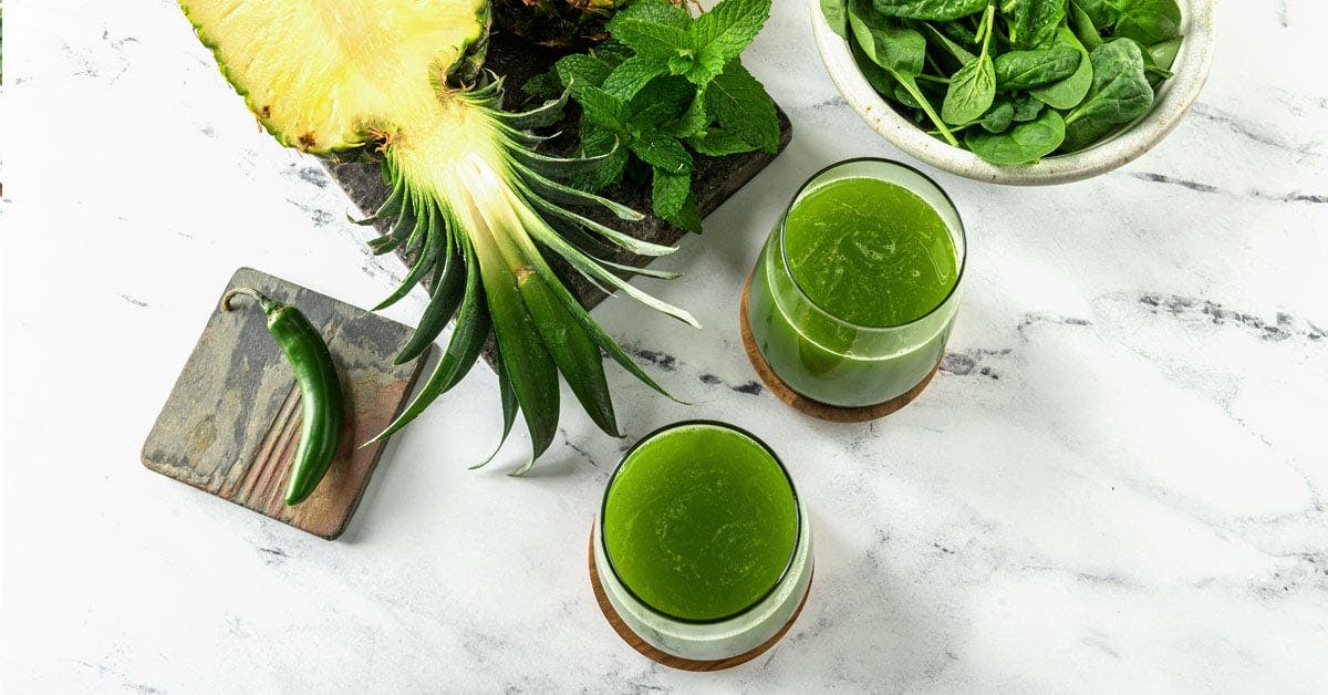 two glasses of pineapple green juice with mint and spinach on a marble table