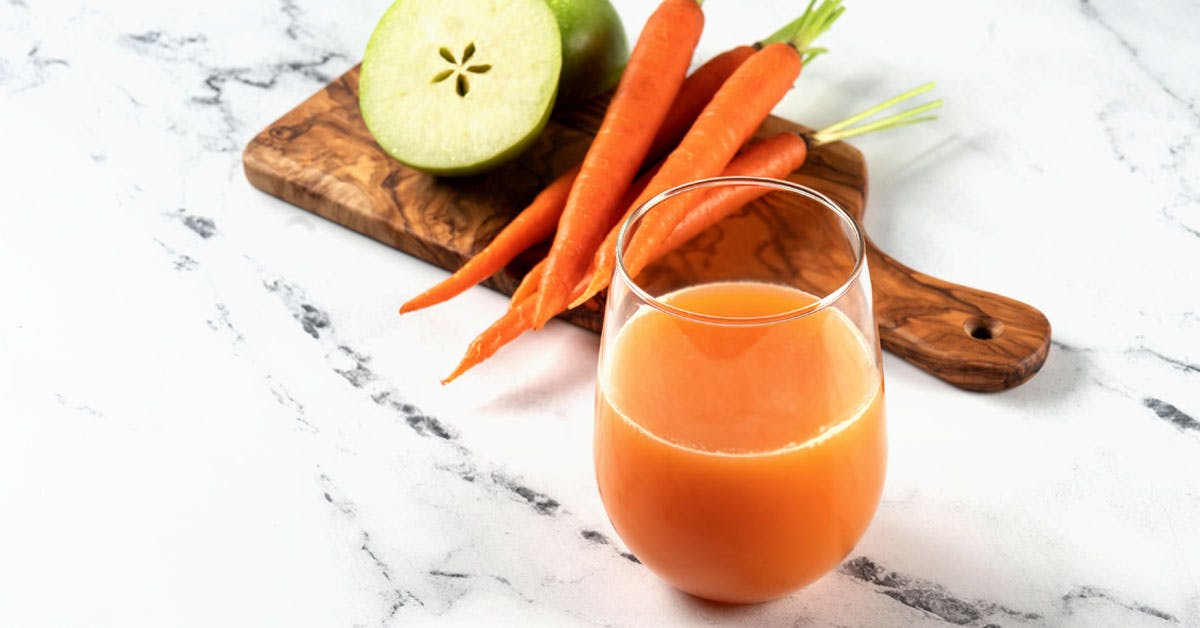 glass of carrot apple juice on a marble countertop