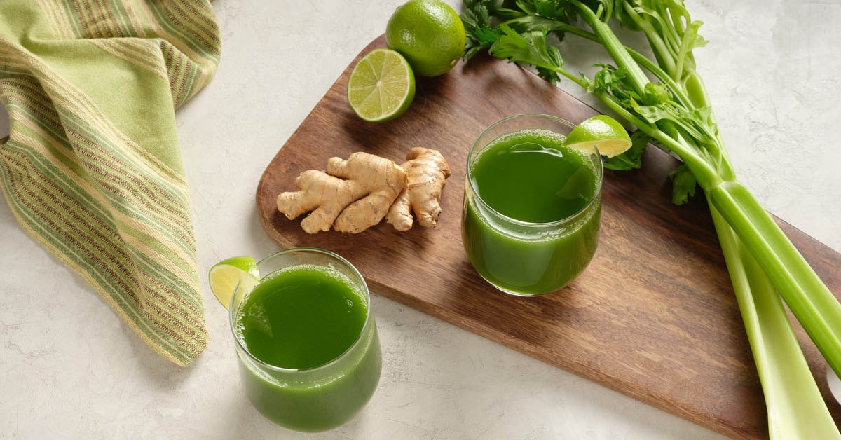 two glasses of celery juice with ingredients on a cutting board