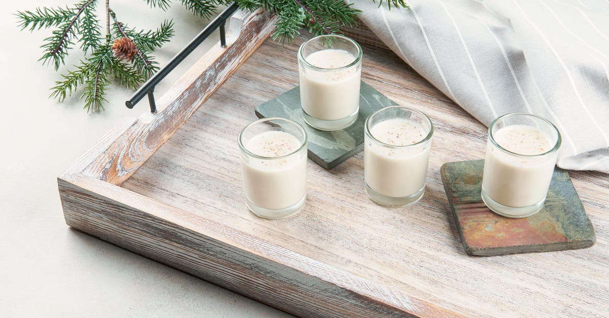 four glasses of vegan eggnog garnished with nutmeg on a wooden serving tray