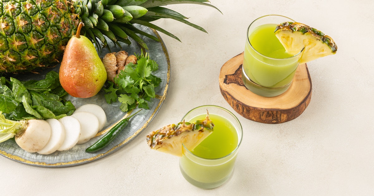 two glasses of pineapple pear juice on a wooden coaster