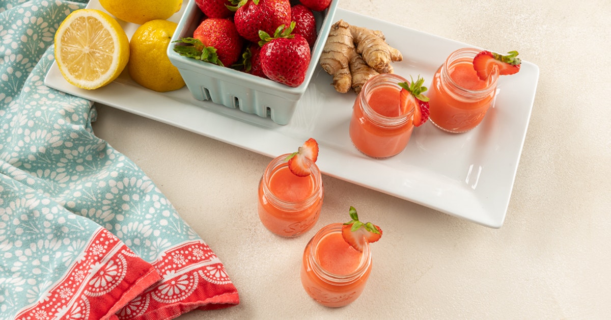 four wellness detox shots with ingredients, strawberry ginger and lemon, on a white serving tray