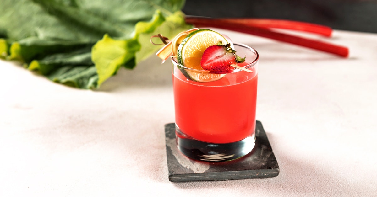 a glass of strawberry rhubarb cold pressed cocktail on a white table