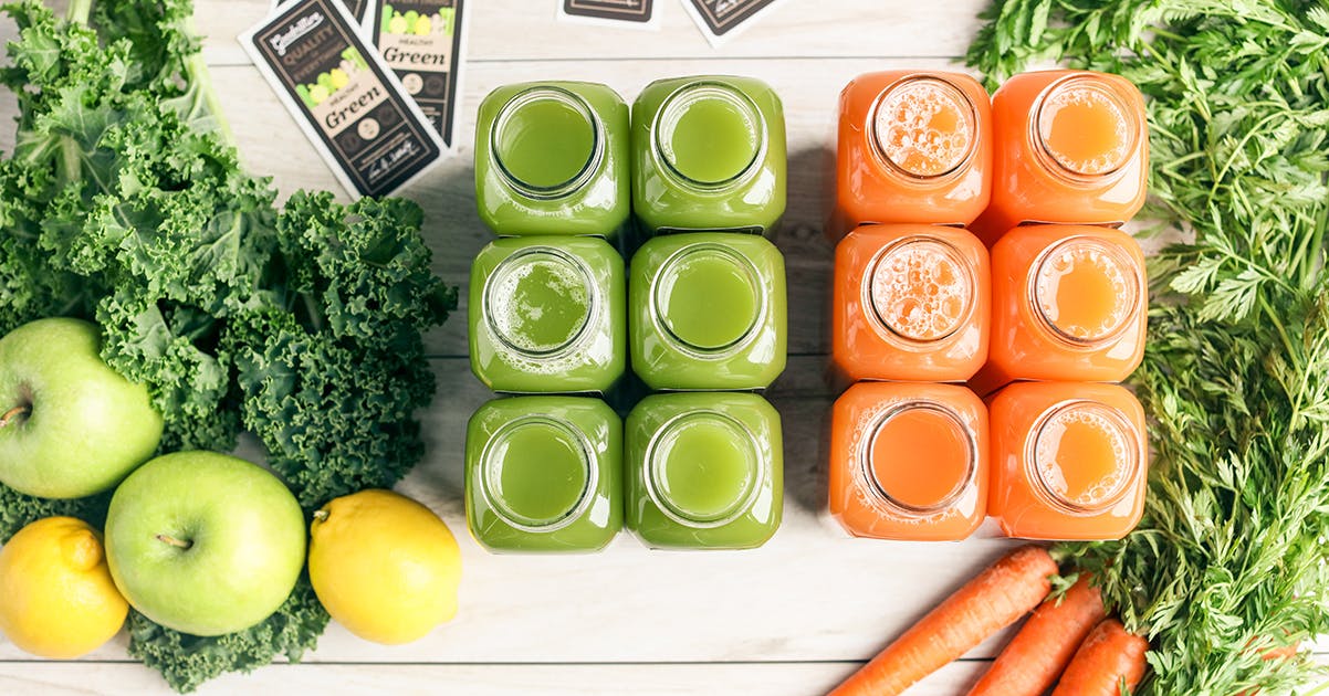 bottles of fresh cold pressed juice surrounded by juice ingredients on a white farm table