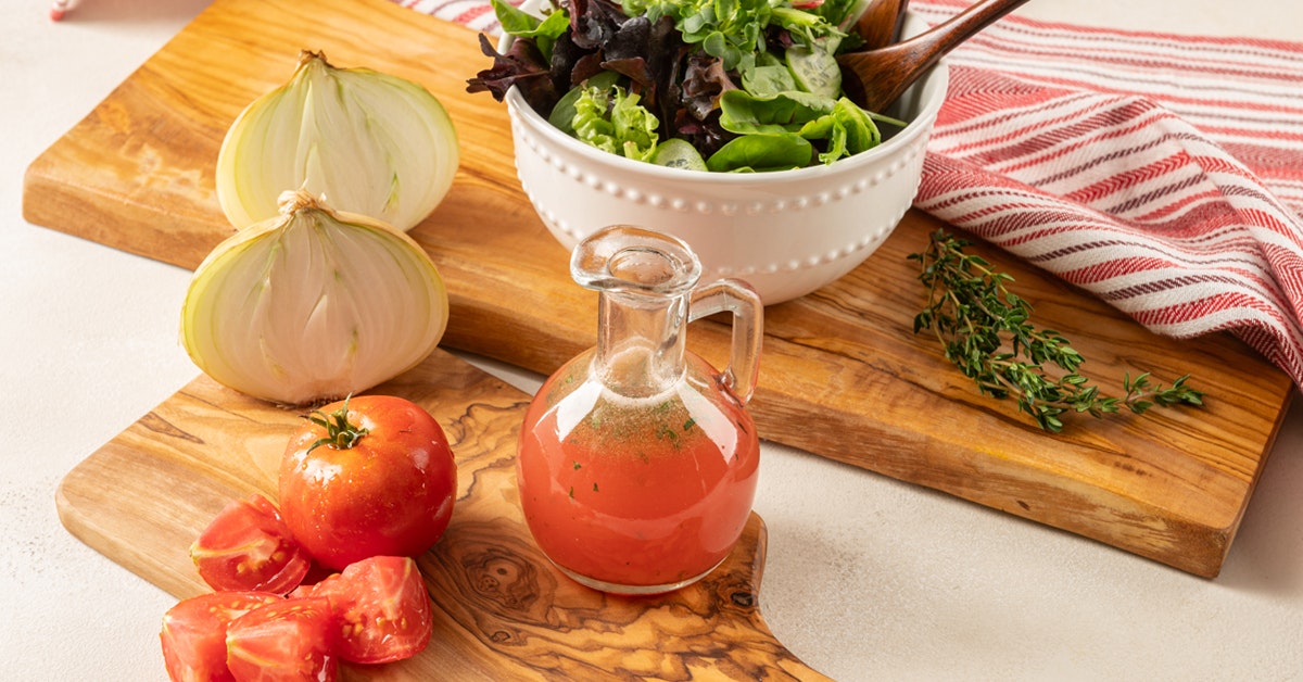 cruet of summer salad dressing and tomatoes, onion, garlic and thyme on a wooden cutting board