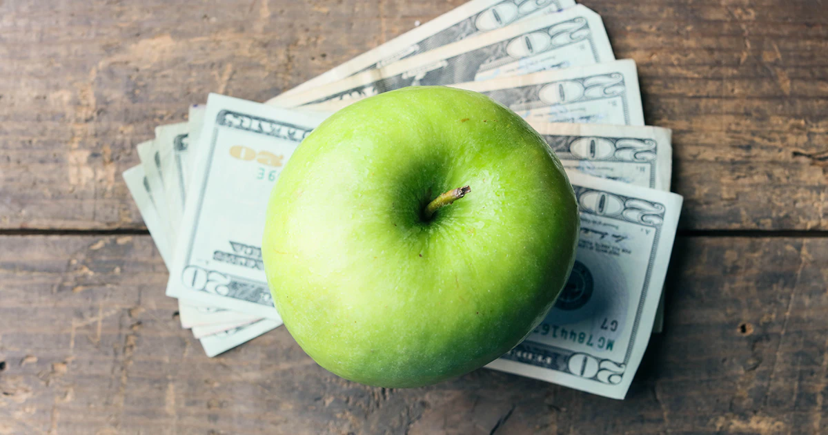 green apple sitting on top of twenty dollar bills on a wooden table