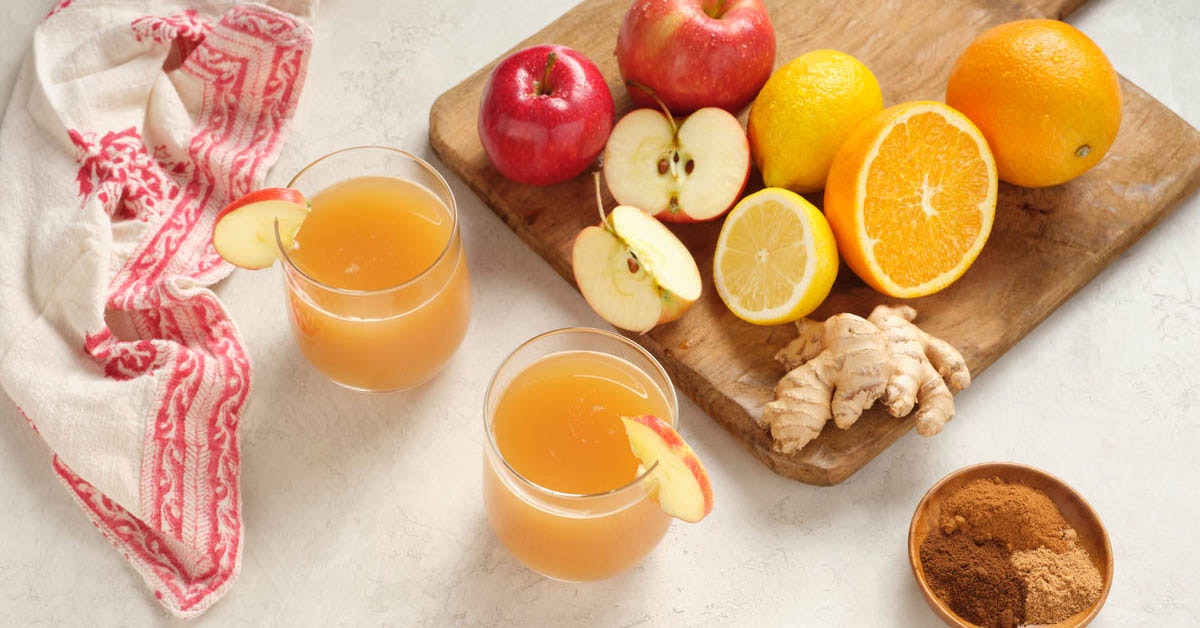two glasses of apple cider with ingredients on a cutting board