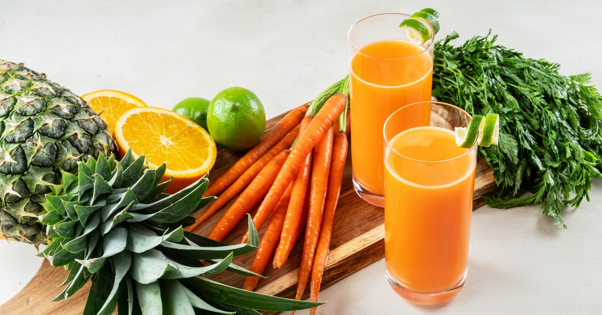 two glasses of carrot orange pineapple juice with recipe ingredients on a table