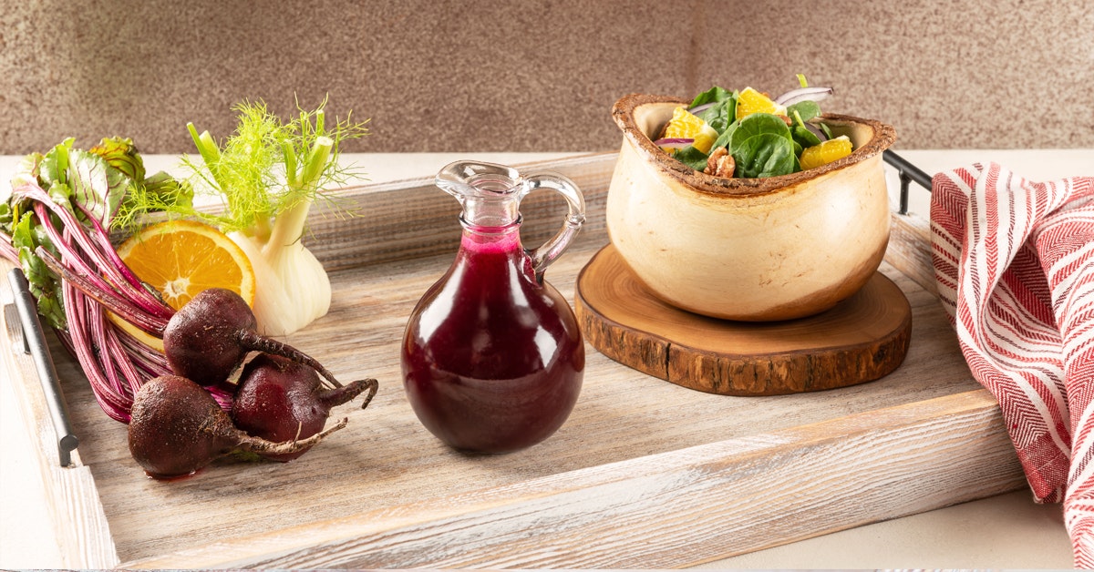 winter beet balsamic salad dressing in a clear cruet surrounded by ingredients on a wooden serving tray