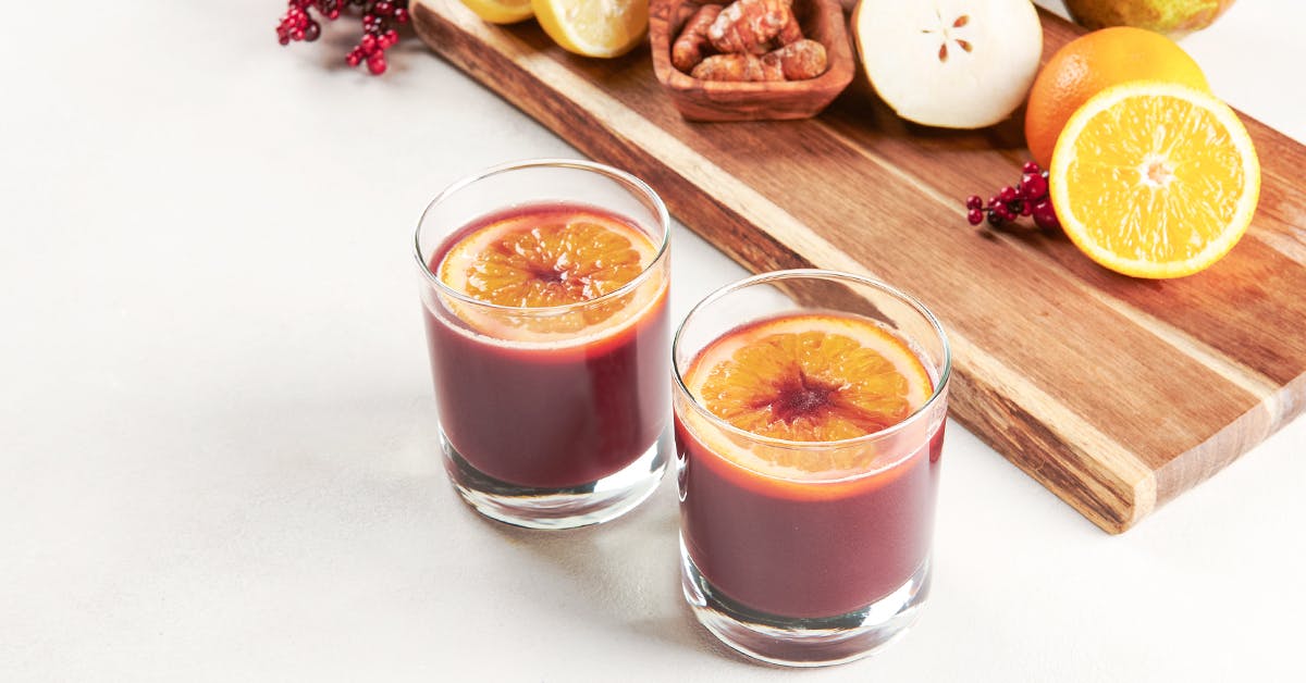 elderberry juice with orange, pear and turmeric on a white surface surrounded by recipe ingredients